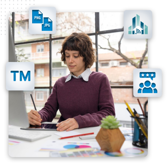 brand logo feat img A woman with short brown hair works at a desk using a tablet and stylus, surrounded by office supplies and icons representing branding solutions, file types, analytics, trademarks, and user groups. Large window and trees are visible behind her.