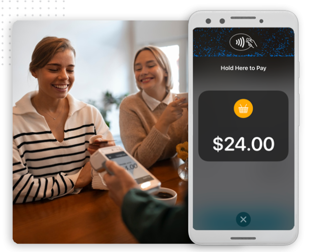 Two women smile at a table as one pays with her smartphone using contactless payment; a mobile screen in the foreground displays a $24.00 purchase—effortless transactions powered by automation company innovations.